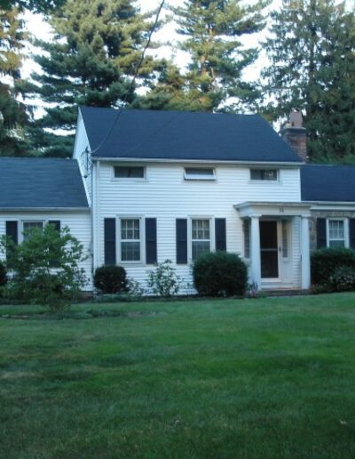 A white house with black shutters and a green lawn.