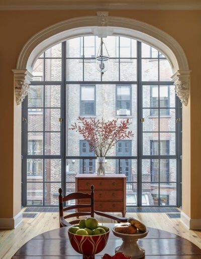 A dining room with arched windows and a bowl of fruit.